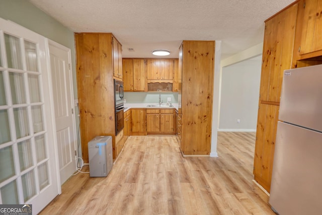 kitchen featuring a textured ceiling, a sink, light wood-style floors, black oven, and freestanding refrigerator