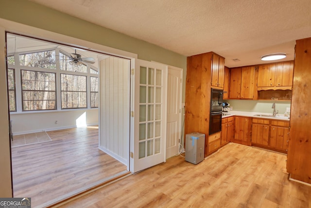 kitchen featuring light wood-type flooring, black appliances, a textured ceiling, and a sink