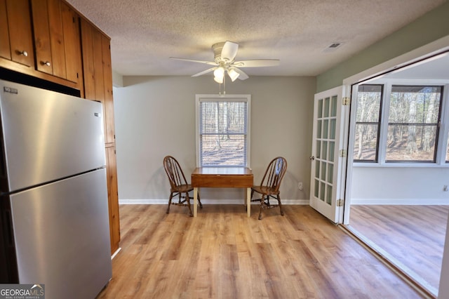 dining space featuring light wood-style floors, ceiling fan, baseboards, and a textured ceiling