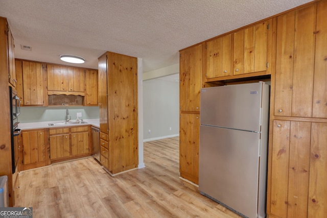 kitchen with a textured ceiling, light wood-style flooring, stainless steel appliances, a sink, and visible vents