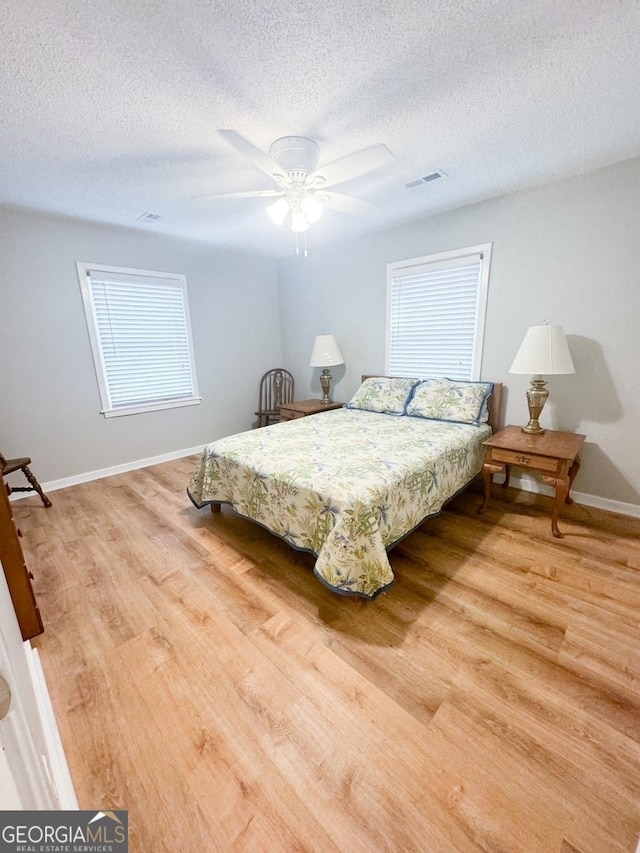 bedroom featuring ceiling fan, light hardwood / wood-style floors, and a textured ceiling