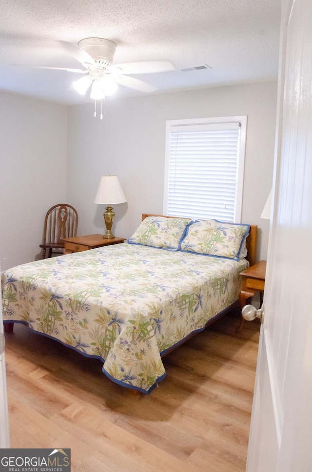 bedroom with ceiling fan, wood-type flooring, and a textured ceiling