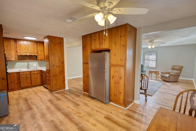 kitchen with a textured ceiling, light wood-style flooring, stainless steel appliances, a sink, and brown cabinets