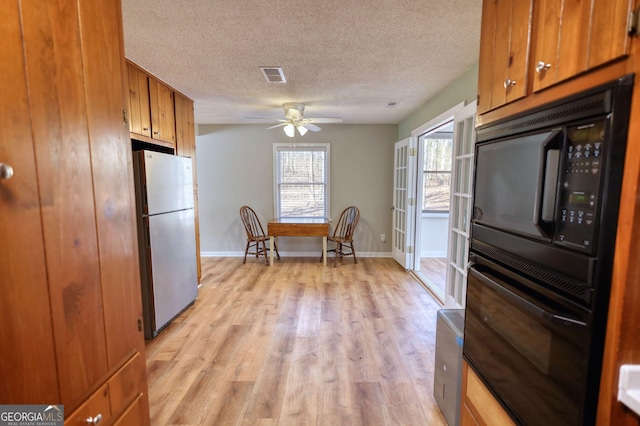 kitchen with brown cabinets, light wood finished floors, visible vents, a textured ceiling, and black appliances