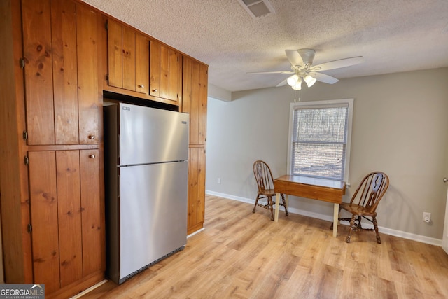 kitchen featuring visible vents, brown cabinetry, ceiling fan, light wood-style flooring, and freestanding refrigerator