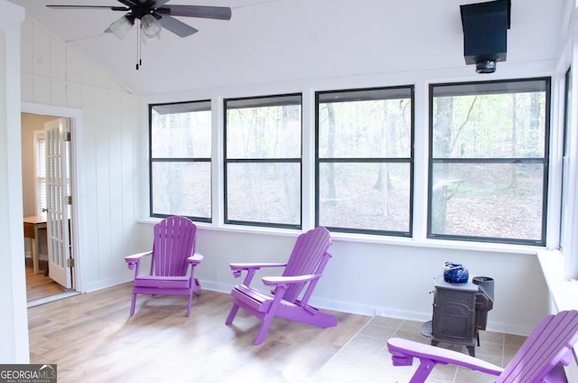 sunroom with a wood stove, plenty of natural light, lofted ceiling, and ceiling fan