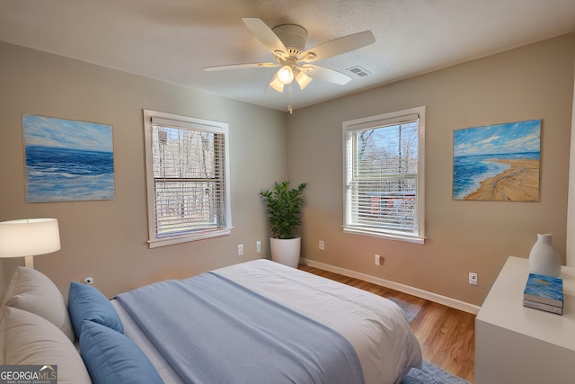 bedroom featuring a ceiling fan, visible vents, baseboards, and wood finished floors