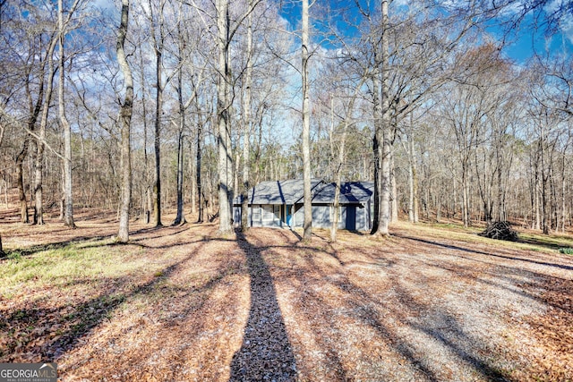 view of front facade with dirt driveway and a view of trees