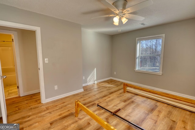 unfurnished room with visible vents, light wood-style flooring, ceiling fan, a textured ceiling, and baseboards