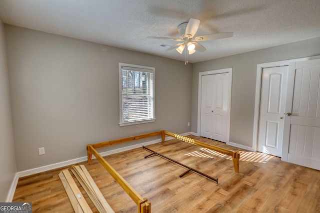 bedroom featuring baseboards, a ceiling fan, wood finished floors, a textured ceiling, and multiple closets