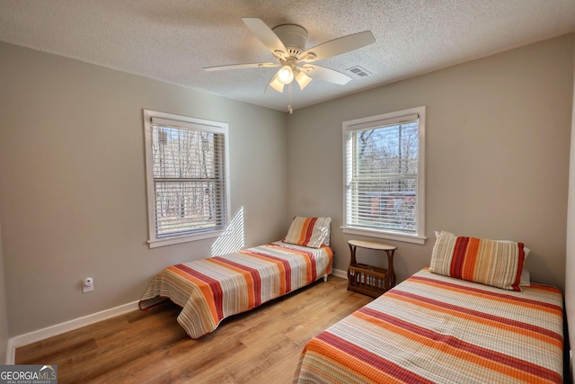 bedroom with a textured ceiling, light wood finished floors, visible vents, and baseboards