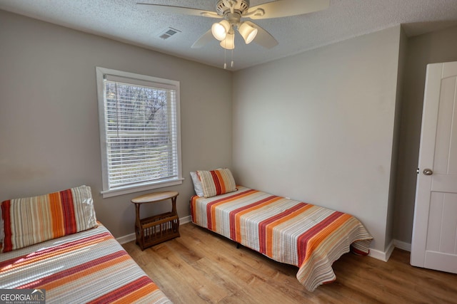 bedroom with visible vents, a textured ceiling, baseboards, and wood finished floors