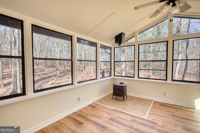 unfurnished sunroom featuring a wood stove, vaulted ceiling, and ceiling fan