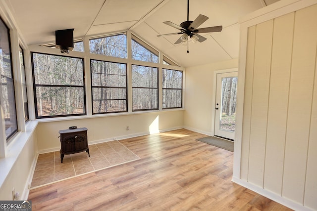 unfurnished sunroom with vaulted ceiling, ceiling fan, and a wood stove