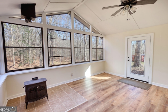 unfurnished sunroom with a wood stove, a ceiling fan, and lofted ceiling