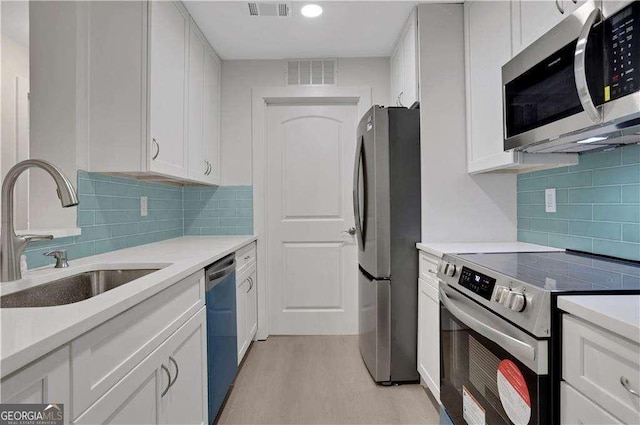 kitchen featuring white cabinetry, sink, stainless steel appliances, backsplash, and light wood-type flooring