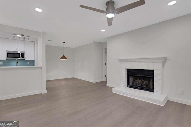 unfurnished living room featuring ceiling fan, rail lighting, light hardwood / wood-style floors, and a brick fireplace