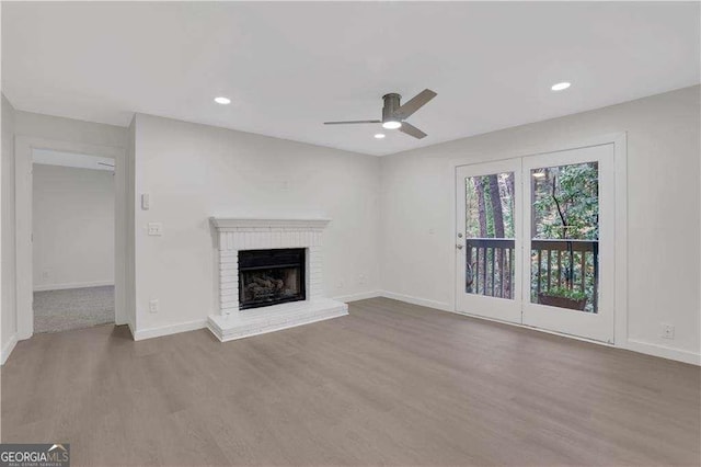 unfurnished living room with ceiling fan, wood-type flooring, and a brick fireplace