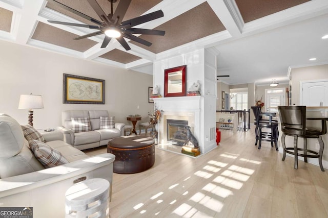 living room featuring beam ceiling, a large fireplace, coffered ceiling, crown molding, and light hardwood / wood-style floors