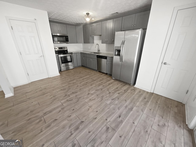 kitchen with gray cabinetry, a textured ceiling, stainless steel appliances, sink, and light hardwood / wood-style floors