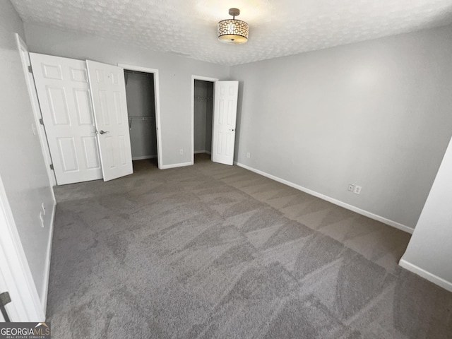 unfurnished bedroom featuring multiple closets, dark carpet, and a textured ceiling