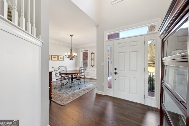 foyer with dark wood-type flooring, a chandelier, and crown molding