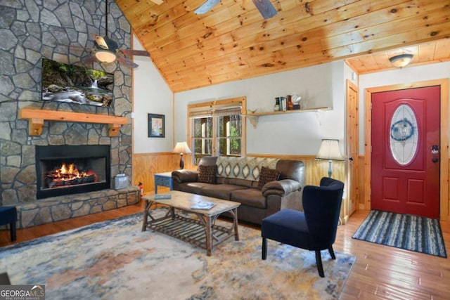 living room featuring ceiling fan, a stone fireplace, wood walls, light hardwood / wood-style floors, and vaulted ceiling