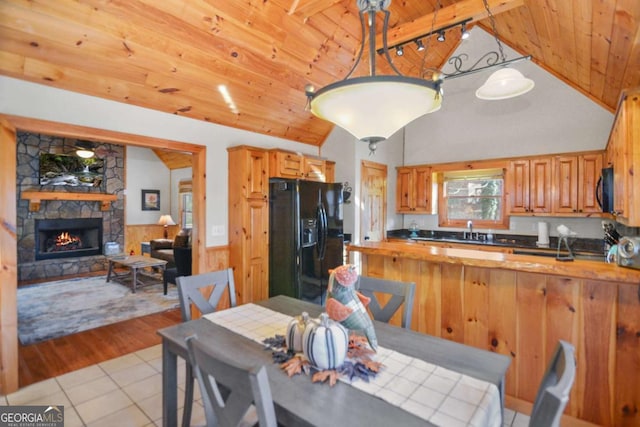 tiled dining room with wood walls, a stone fireplace, sink, vaulted ceiling, and wood ceiling