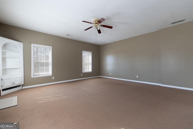 carpeted empty room featuring a ceiling fan, visible vents, and baseboards