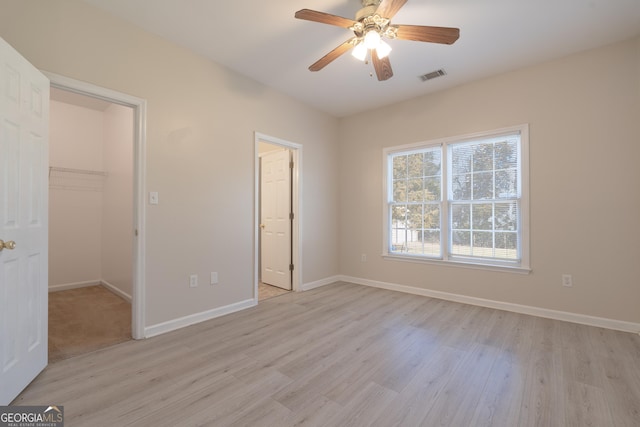 unfurnished bedroom featuring a walk in closet, a closet, visible vents, light wood-style flooring, and baseboards