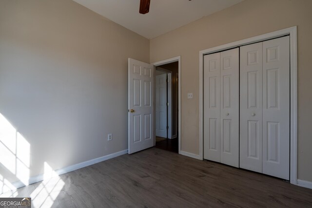 unfurnished bedroom featuring dark wood-type flooring, a closet, a ceiling fan, and baseboards