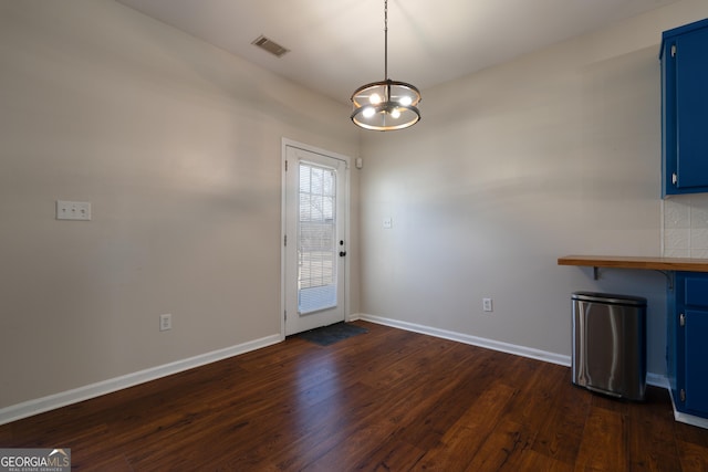 doorway to outside featuring a notable chandelier, dark wood-type flooring, visible vents, and baseboards