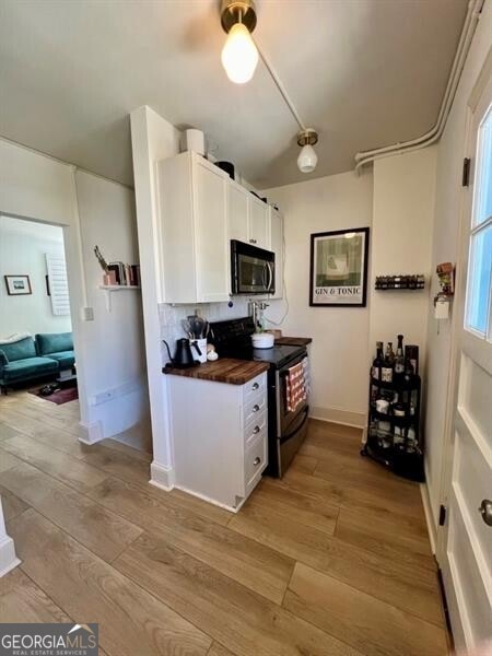 kitchen with white cabinetry, butcher block counters, decorative backsplash, black electric range, and light hardwood / wood-style flooring