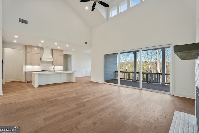 unfurnished living room featuring a towering ceiling, sink, ceiling fan, and light wood-type flooring