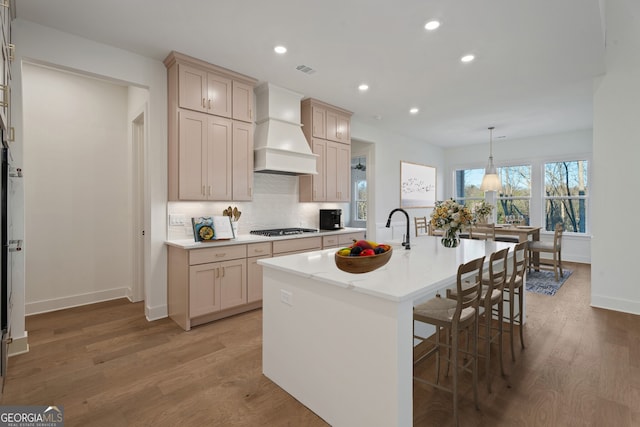 kitchen featuring pendant lighting, custom range hood, a center island with sink, and sink