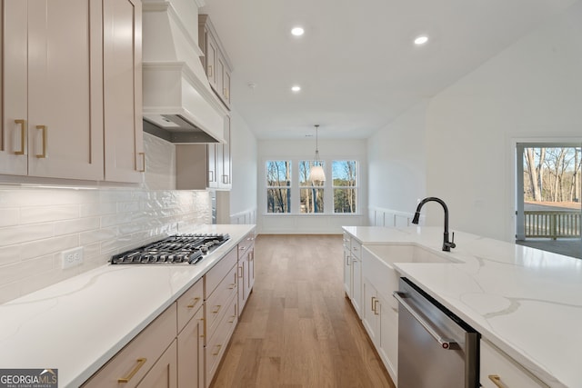 kitchen featuring appliances with stainless steel finishes, decorative light fixtures, sink, custom exhaust hood, and light wood-type flooring