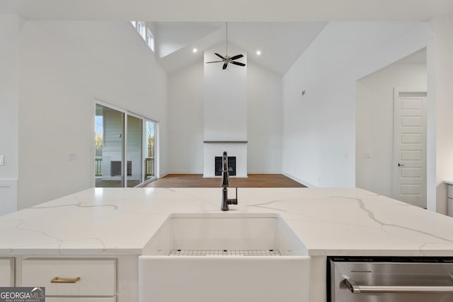 kitchen with sink, white cabinetry, light stone counters, high vaulted ceiling, and ceiling fan