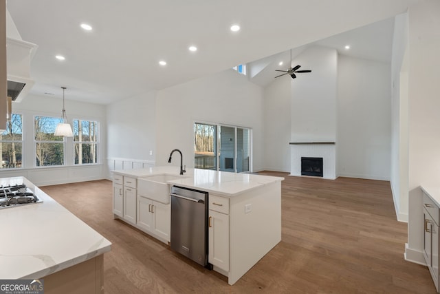 kitchen with pendant lighting, a fireplace, white cabinets, a kitchen island with sink, and stainless steel appliances