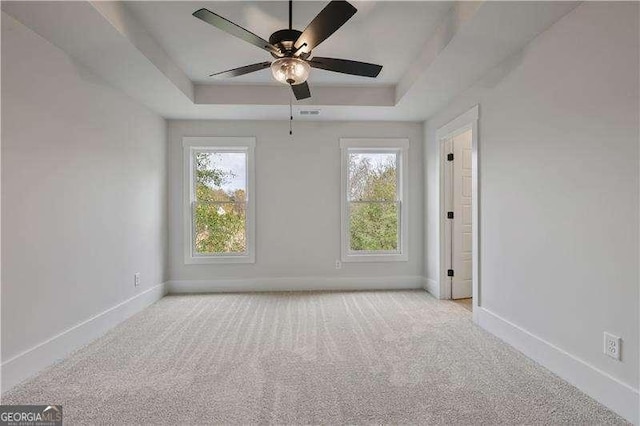 carpeted empty room with a tray ceiling, ceiling fan, and plenty of natural light