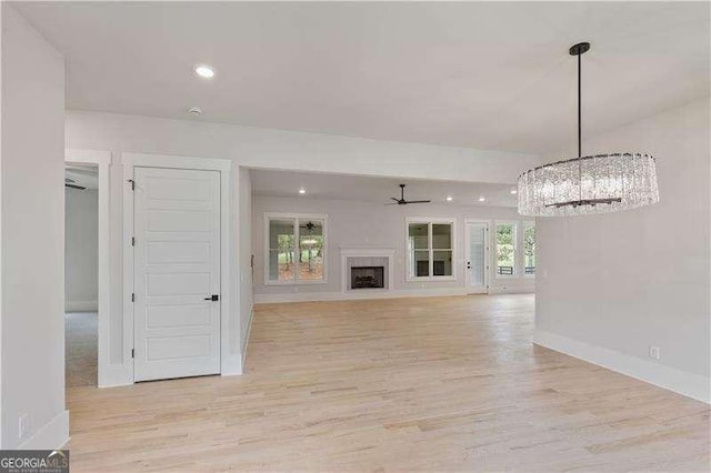 unfurnished living room featuring light hardwood / wood-style flooring and ceiling fan with notable chandelier