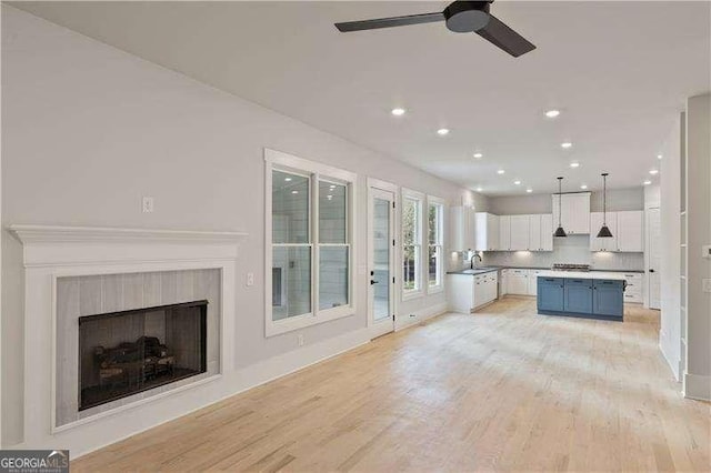 unfurnished living room with light wood-type flooring, ceiling fan, and sink