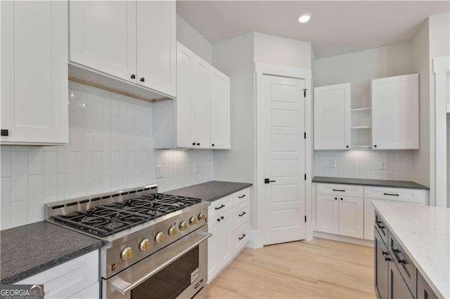 kitchen featuring backsplash, light stone counters, stainless steel range, light hardwood / wood-style flooring, and white cabinets