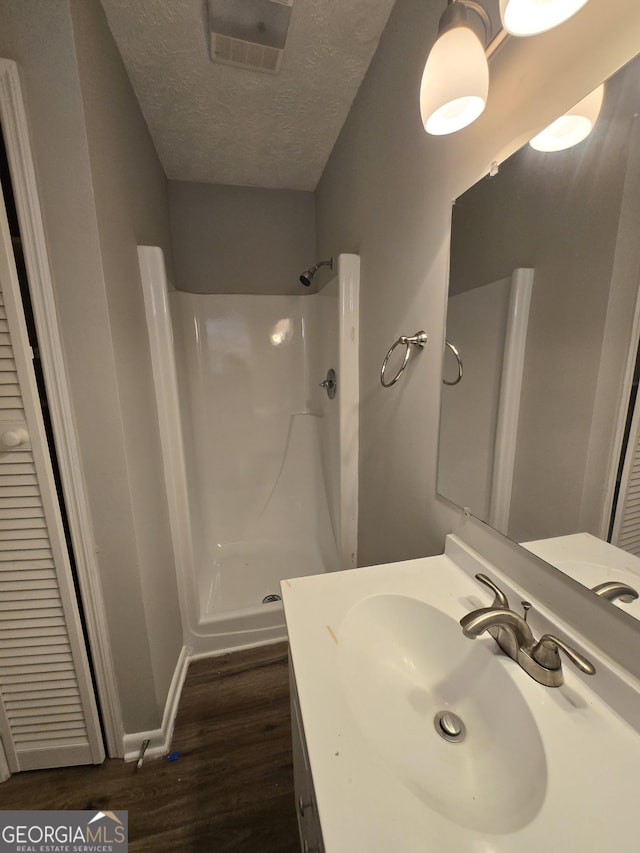 bathroom with a textured ceiling, hardwood / wood-style flooring, walk in shower, and sink