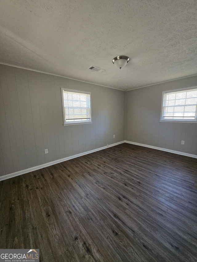 unfurnished room featuring a textured ceiling, dark hardwood / wood-style flooring, a healthy amount of sunlight, and wood walls