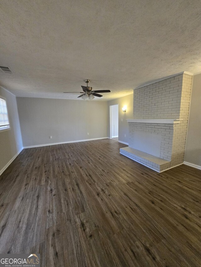 unfurnished living room featuring a fireplace, a textured ceiling, dark hardwood / wood-style floors, and ceiling fan