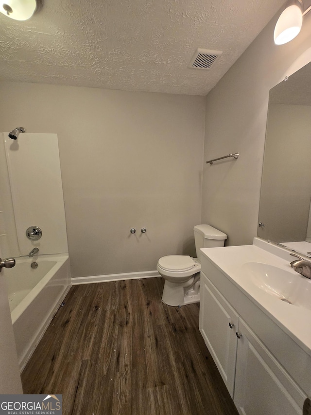 full bathroom with bathing tub / shower combination, hardwood / wood-style floors, a textured ceiling, toilet, and vanity