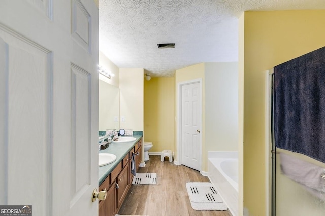 bathroom featuring a bathtub, vanity, toilet, a textured ceiling, and wood-type flooring