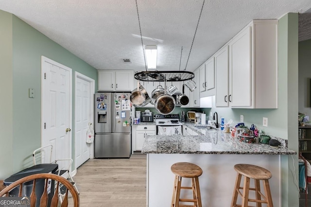 kitchen with stainless steel refrigerator with ice dispenser, a textured ceiling, sink, white cabinets, and white range with electric cooktop