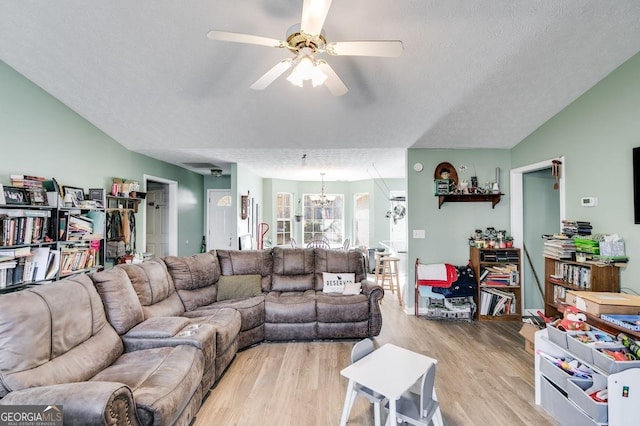 living room with ceiling fan with notable chandelier, light hardwood / wood-style floors, and a textured ceiling