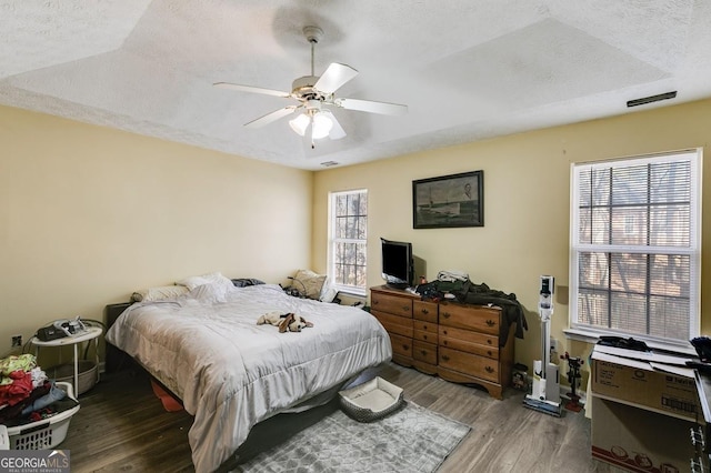 bedroom featuring a textured ceiling, hardwood / wood-style flooring, a raised ceiling, and ceiling fan